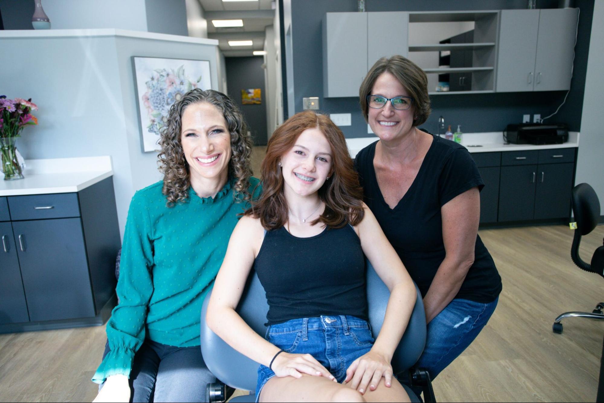 Teen patient with long auburn hair smiling between two staff members at Rhoads Orthodontics, Dr. Stephanie Rhoads’ Mars PA orthodontics office